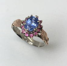 Load image into Gallery viewer, large oval cornflower blue and 12 vibrant pink sapphire in a halo around it, white gold ring with rose gold fabricated leaves on the band
