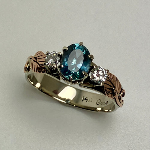 white gold ring with blue sapphire and 2 diamonds with rose gold leaves and vines