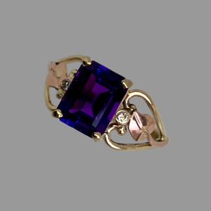 emerald cut amethyst in prong setting, 2 bezel set diamonds and rose gold leaves on the sides