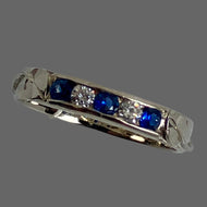 Narrow 14K white gold band with 3 round blue sapphires and 2 round diamonds, leaf and vine on sodes