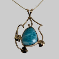 freeform ocean blue/green center stone, bezel set with 3 leaves and swirly vines around it, pendant in 14K yellow gold