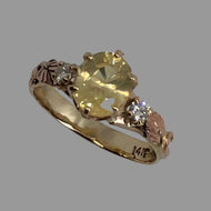 14K gold ring featuring an oval-cut buttery yellow Sapphire and two small natural Diamonds with 14K rose gold leaves and vines.
