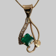 A 14k yellow gold pendant necklace featuring a prominent square emerald, accented by a curved pavé-set row of diamonds