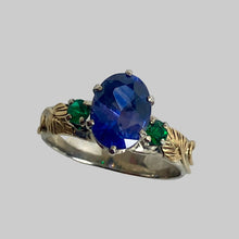 Load image into Gallery viewer, 14K white and 18K yellow gold ring featuring a large oval purple/blue sapphire center stone, accented by two round emeralds and  leaves and vines
