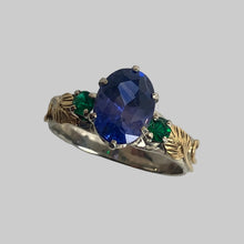 Load image into Gallery viewer, Large blue/puprle dichroic sapphire set with a pair of fine round emeralds in a 14K white band with 18K yellow goldleaves and vines.
